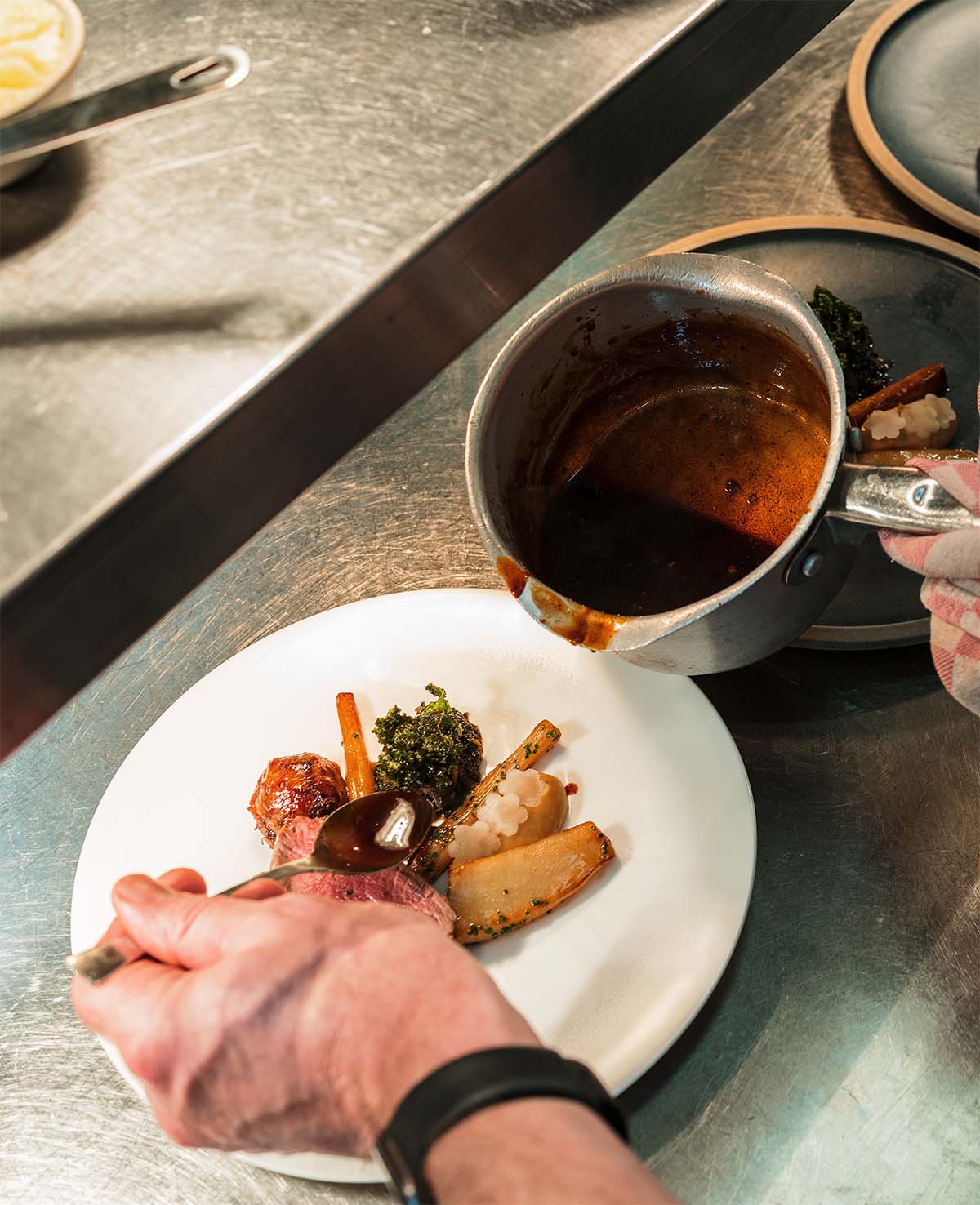 Plating-up-dish-sauce-Peacock-Rowsley Finishing the plating up of a dish with sauce in the kitchen